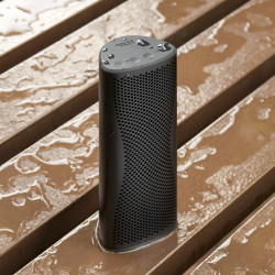 KEF MUO enceinte Bluetooth noire étanche, posée sur planches de bois mouillées avec gouttes d'eau