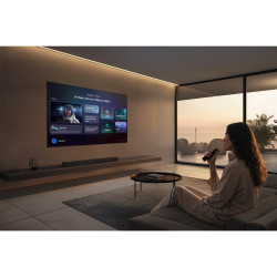 SAMSUNG TQ65S92H TV OLED 65 pouces, écran mural en salon avec interface vocale et femme tenant télécommande